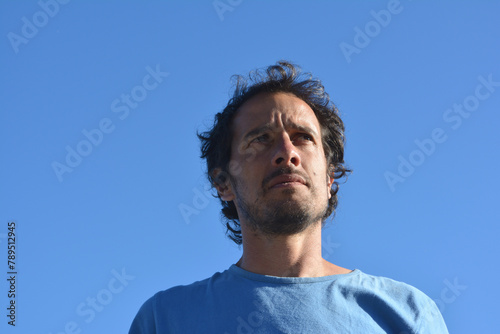 pensive brown haired Latin American man outdoors with blue sky in the background