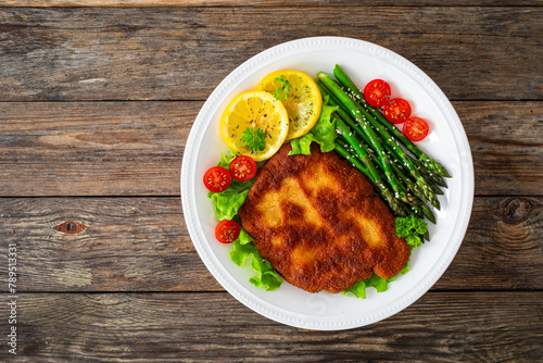 Crispy breaded fried pork chop, green asparagus and fresh vegetables on wooden table 