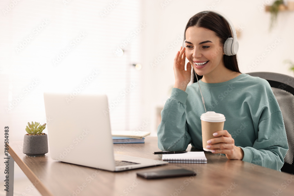 Young woman in headphones watching webinar at table in room Young woman in headphones watching webinar at table in room
