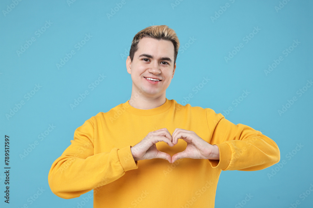 Naklejka premium Young man showing heart gesture with hands on light blue background