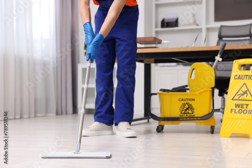 Cleaning service worker washing floor with mop  closeup. Bucket with wet floor sign in office
