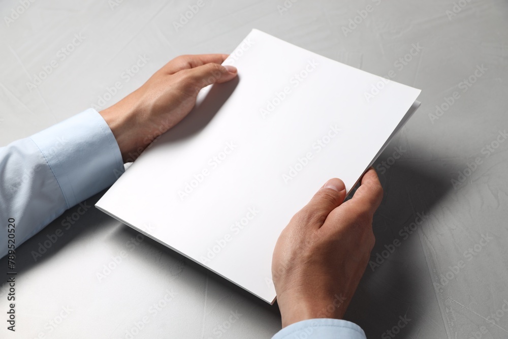 Man holding blank notebook at light grey table, closeup. Mockup for design Man holding blank notebook at light grey table, closeup. Mockup for design