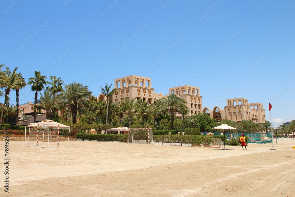 A beach with a fountain and palm trees and a large building in the background