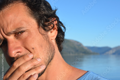 portrait of brown haired man thinking outdoors with lake and mountains