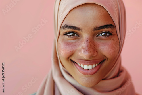 Portrait of a young Muslim woman smiling, wearing a hijab against a solid color background