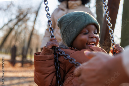 Boy having fun with parents while playing on swing at park photo