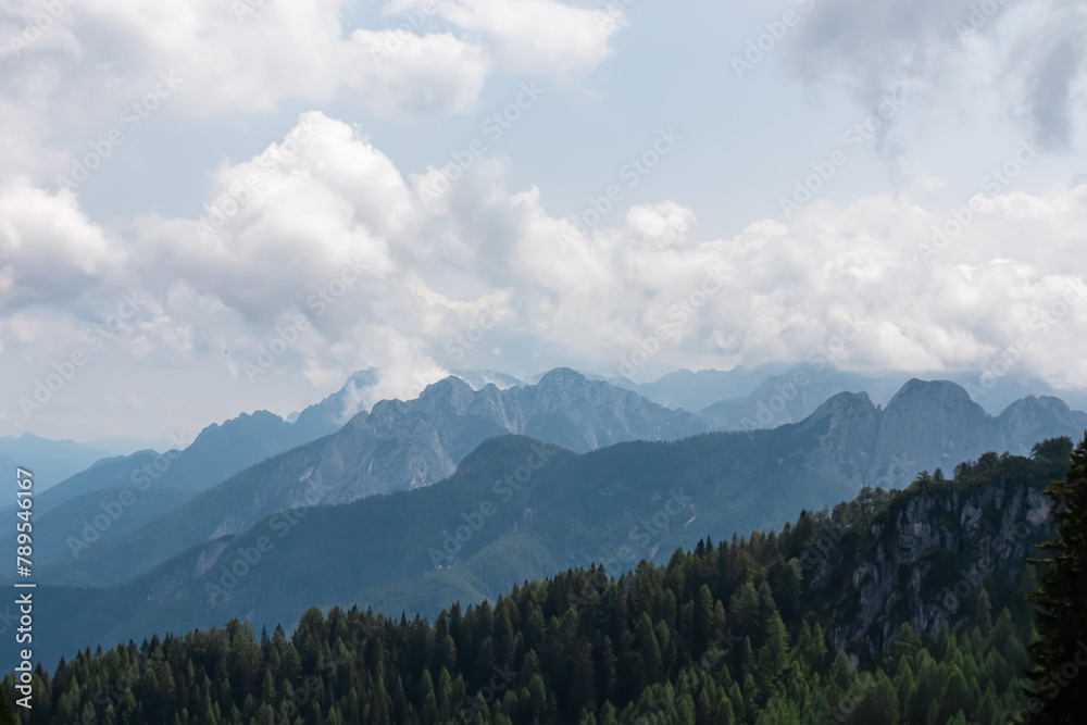 Panoramic view from Monte Lussari in Camporosso, Friuli Venezia Giulia, Italy. Looking at majestic mountain peaks of Julian Alps and Karawanks, border to Austria Slovenia. Misty atmosphere in nature