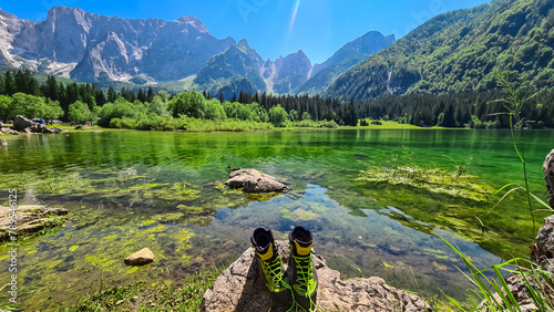 Hiking shoes with panoramic view of Superior Fusine alpine Lake (Laghi di Fusine) with majestic Mount Mangart in back in Tarvisio, Friuli Venezia Giulia, Italy. Water Reflection in tranquil atmosphere photo