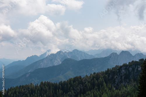 Panoramic view from Monte Lussari in Camporosso, Friuli Venezia Giulia, Italy. Looking at majestic mountain peaks of Julian Alps and Karawanks, border to Austria Slovenia. Misty atmosphere in nature