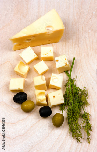 Hard yellow cheese, black and green olives, a sprig of dill on a wooden board. Flat Lay