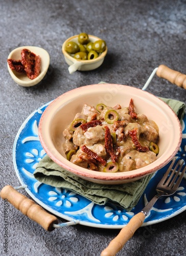 A hot dish, stewed beef with dried tomatoes and olives in a clay bowl on a blue meallic tray on a dark concrete background. Beef recipes. photo