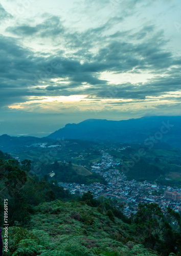 Wide panorama of the colonial village, pueblo, of Jerico, Jericó, Antioquia, Colombia, with an evening orange sky and the Andes Mountains in the background. From the Cerro las Nubes.