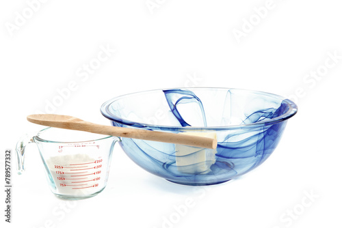 A blue glass mixing bowl with butter and a measuring cup of flour isolated on white