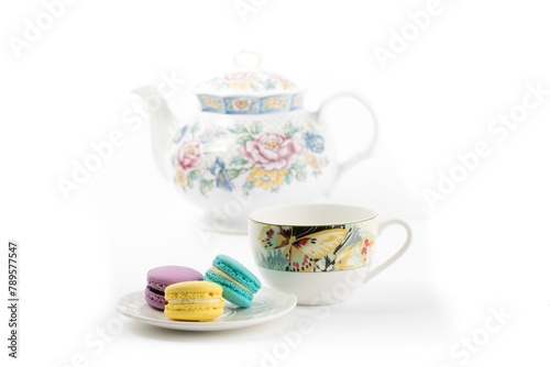 a plate of colorful macaroon or meringue cookies with a teacup and a teapot on a white background