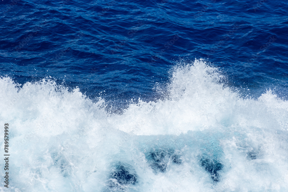 Blue surface of the ocean with splashing white wave. Abstract background.