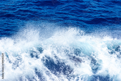 Blue surface of the ocean with splashing white wave. Abstract background.