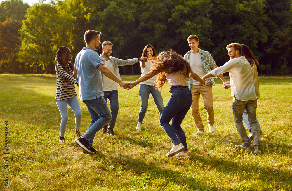 Group of cheerful and carefree best friends in park are circling together holding hands. Young people in casual clothes gathered together for weekend in park in summer and dance in circle. Group of cheerful and carefree best friends in park are circling together holding hands. Young people in casual clothes gathered together for weekend in park in summer and dance in circle.