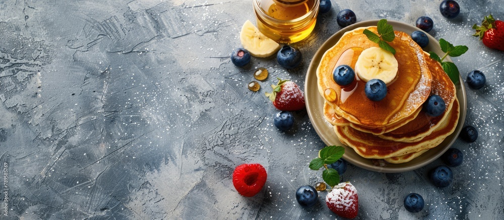 Buttermilk Pancakes topped with banana, blueberries, and honey, placed on a concrete surface with space for text. Overhead shot of pancakes with berries on a table.