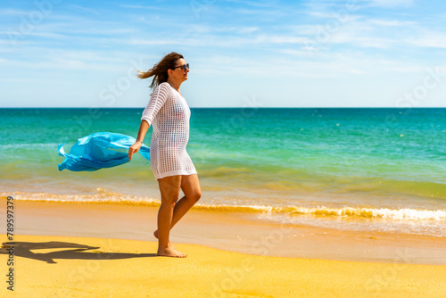 Beautiful woman walking on sunny beach holding shawl
