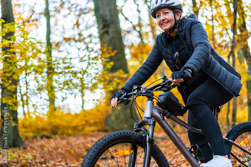 Obraz premium Woman riding bicycle in city forest in autumnal scenery 