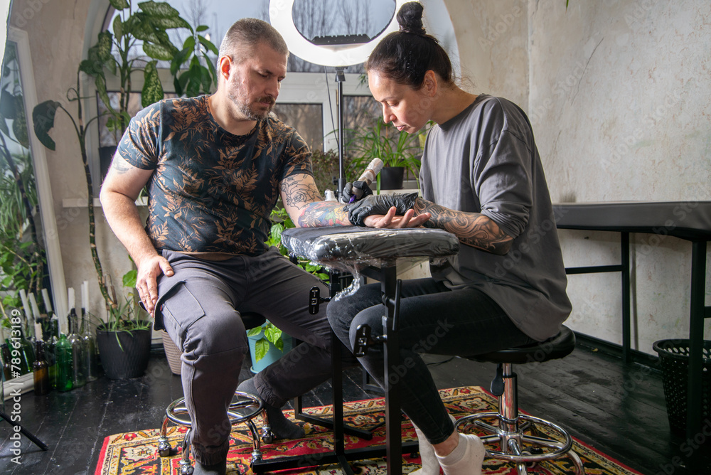 Woman tattoo artist tattooing man in salon Woman tattoo artist tattooing man in salon