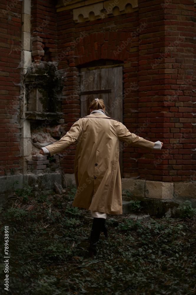 a woman in a raincoat walking near the old
building a woman in a raincoat walking near the old
building