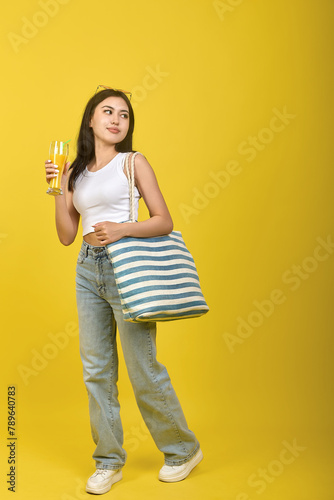 Beautiful confident Asian woman stylishly dressed with a striped bag on her shoulder looks away and smiles. On a yellow background, a charming girl in a white T-shirt and jeans photo