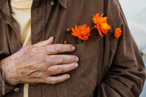 An elderly woman holds orange flowers tucked into her shirt pocket