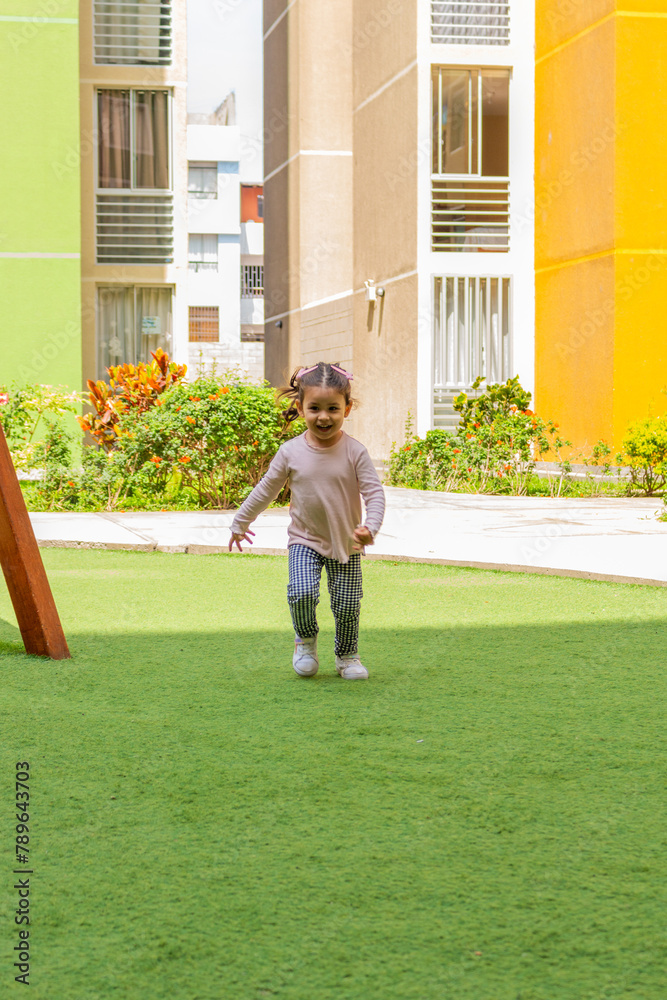 Una linda niña de dos años sonriente corre en el patio de juegos de un condominio.