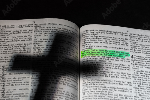 An open bible with a shadow of a cross and a highlighted verse. photo