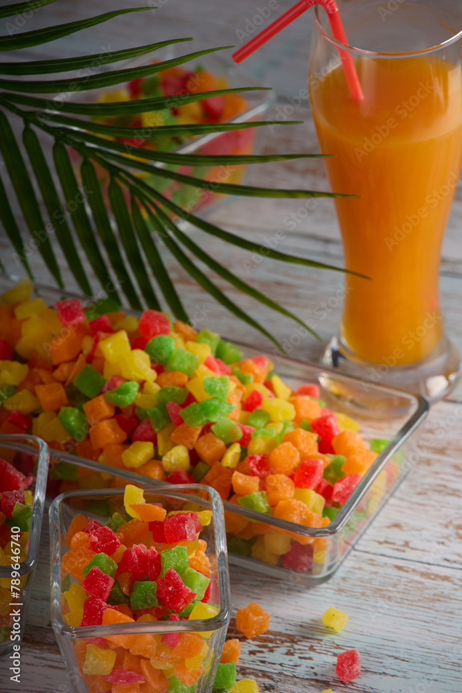 Vertical photo with the image of a glass with delicious freshly squeezed juice standing on the table along with candied fruits in a dish.