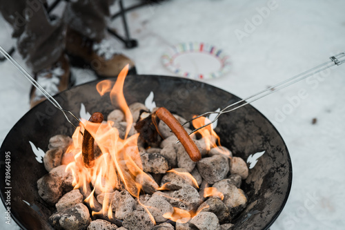 Hot dogs grilled over a portable fire pit in the snow. photo