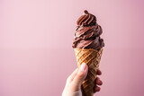 woman's hand holding a chocolate ice cream cone on pink background