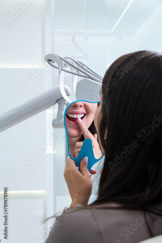 Unrecognizable woman checking and pointing at her teeth in a mirror after treatment in a dentistry clinic. Dental whitening and smile concept.