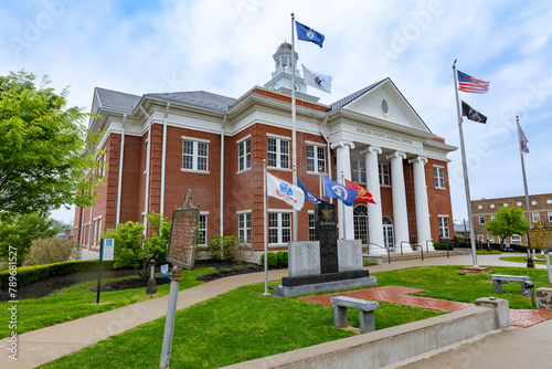 Numerous flags flutter proudly in front of a governmental edifice within a quaint rural town in the United States of America.