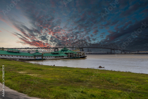 The Horace Wilkinson Bridge over the flowing waters off the Mississippi River with boats on the water, lush green grass and clouds at Louisiana Memorial Plaza in Baton Rouge Louisiana USA
