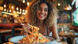A woman with curly hair smiling while eating pasta in a restaurant, AI