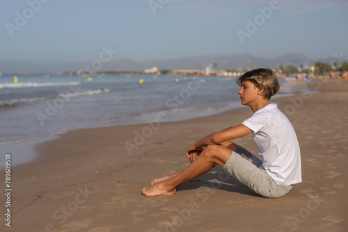 Handsome teenager boy sitting at the beach and enjoy a summer vacation.