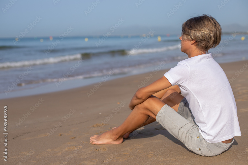 Close up handsome teenager boy sitting at the beach and enjoy a summer vacation.