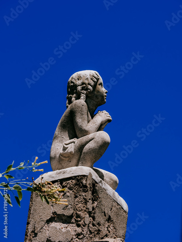 Escultura de niño en cuclillas con cielo despejado de fondo, capturando inocencia y serenidad photo