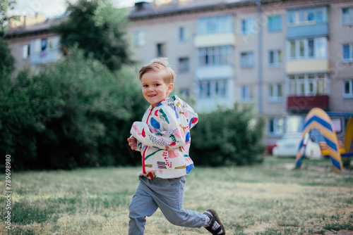 A young 4 years old boy posing outside, wearing colorfull jacket