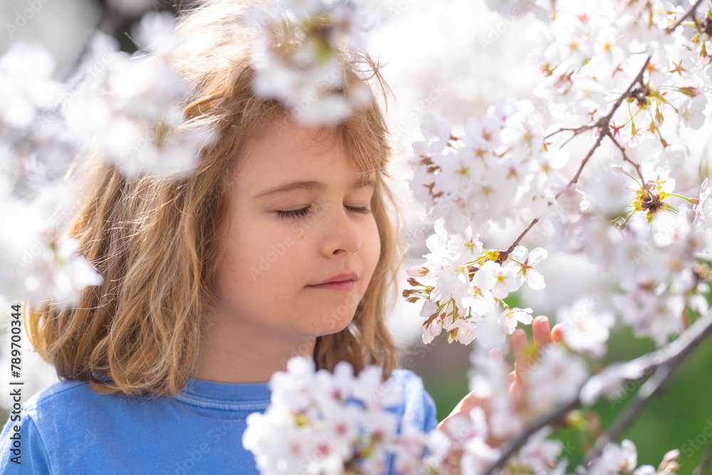 Happy spring. Close up portrait of smiling child face near white cherry blossom tree, spring flowers. Kid among branches of spring tree in blossoms. Cute kids face surrounded spring blossom flowers.