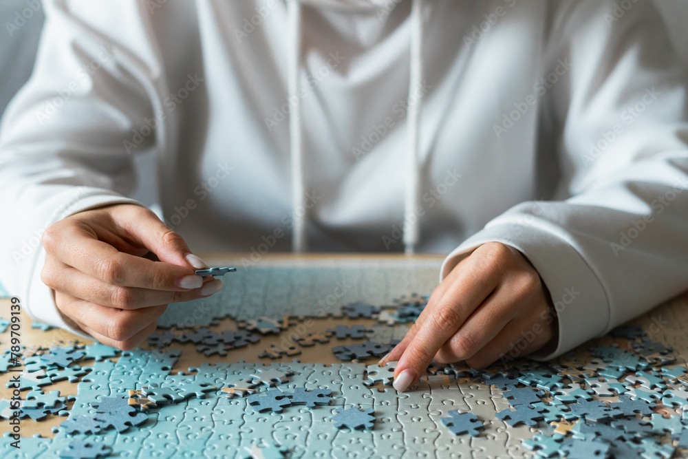 Anonymous woman in white hoody assembling a puzzle at home Anonymous woman in white hoody assembling a puzzle at home