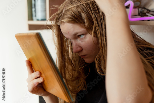 Teen girl sadly examines acne in mirror, skin facial concerns photo