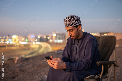 Arab man browsing mobile phone while sitting on chair at hill photo