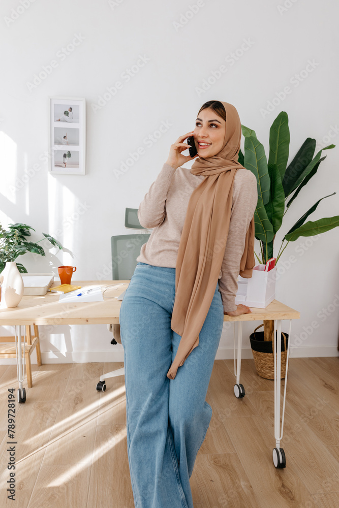 Smiling woman talking on smartphone while leaning on table at home Smiling woman talking on smartphone while leaning on table at home