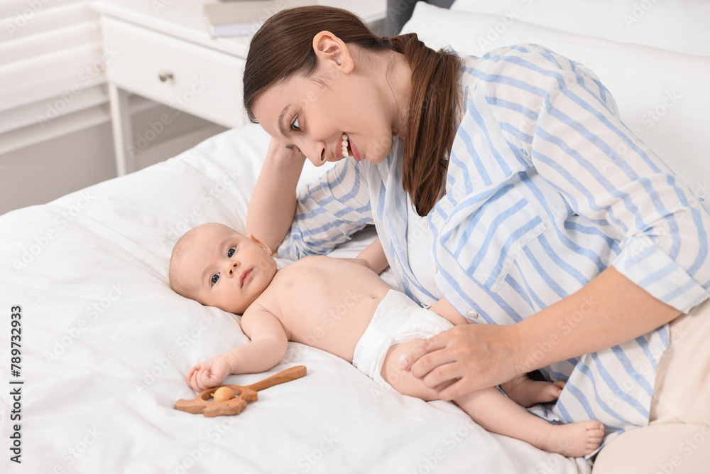 Happy young woman applying body cream onto baby`s skin on bed Happy young woman applying body cream onto baby`s skin on bed