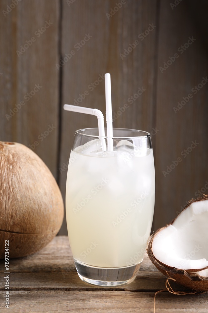Glass of coconut water, ice cubes and nuts on wooden table - obrazy, fototapety, plakaty 