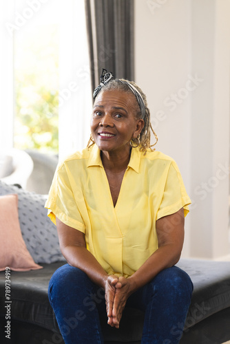A senior African American woman sitting at home, wearing a yellow shirt and jeans, on a video call