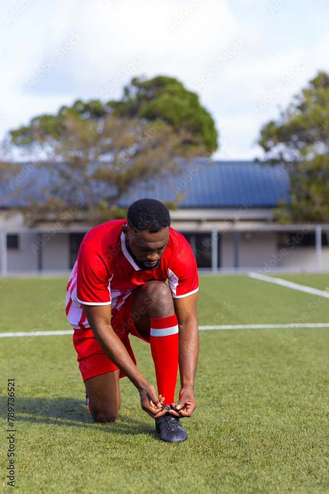 African American young male athlete tying his shoelaces on a soccer field outdoors, copy space